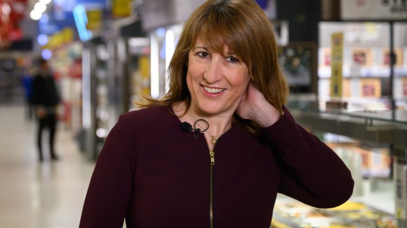 Rachel Reeves discussing economic policies in a supermarket aisle with diverse products on shelves in the background.
