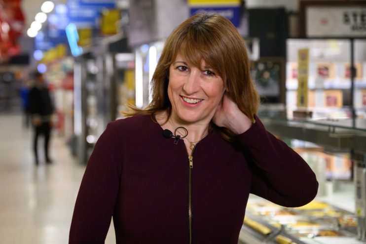Rachel Reeves discussing economic policies in a supermarket aisle with diverse products on shelves in the background.