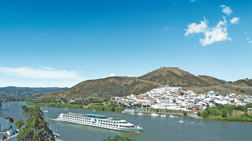 Luxury cruise ship docked at a sunny Spanish port, surrounded by clear blue waters and scenic coastal views.