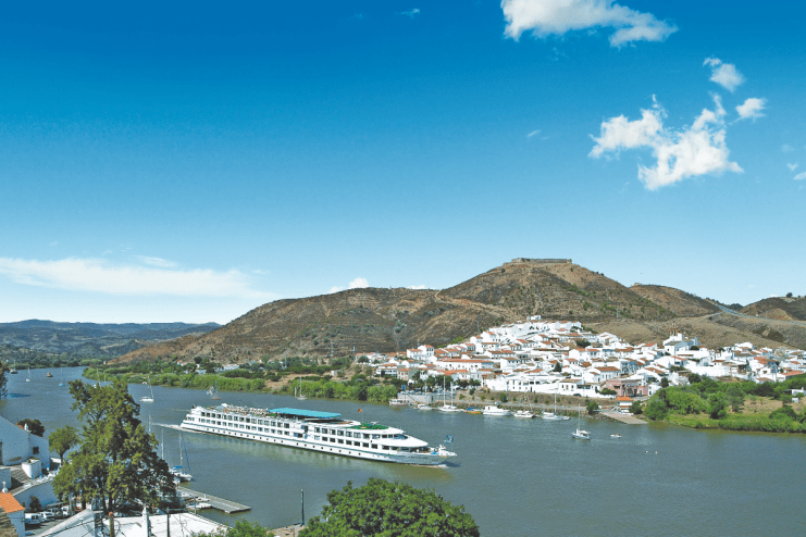 Luxury cruise ship docked at a sunny Spanish port, surrounded by clear blue waters and scenic coastal views.