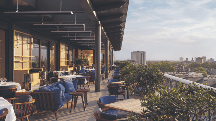 London skyline view from a rooftop bar in Kensington and Chelsea, featuring stylish seating and vibrant evening atmosphere
