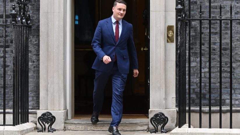 Wes Streeting addressing media at a public event, wearing a suit and tie, with a focused expression and microphones visible
