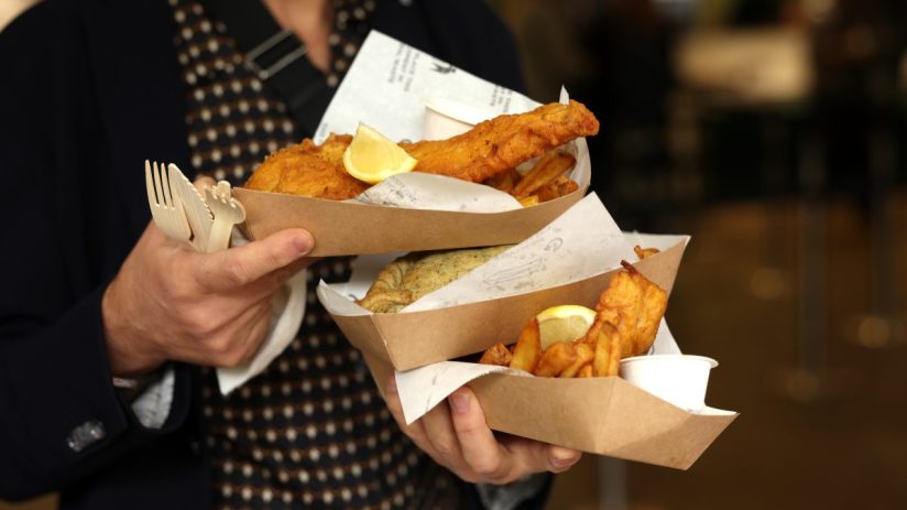 Crispy golden fish and chips served on a newspaper with lemon wedges and tartar sauce in a traditional British setting