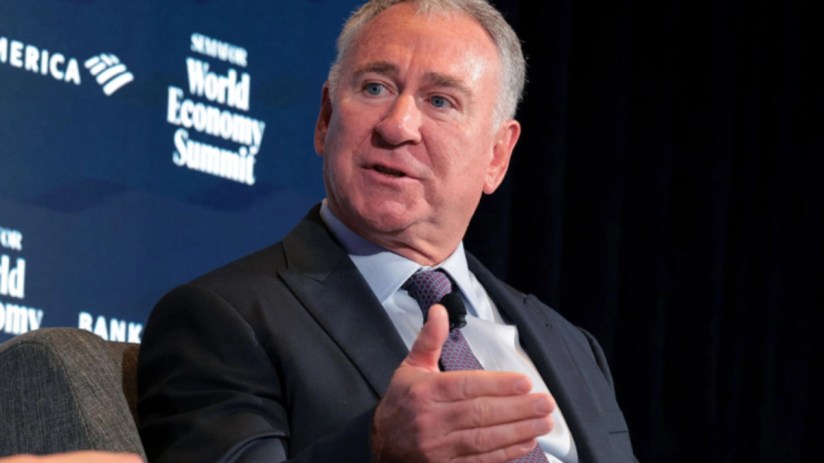 Ken Griffin speaking at a business conference representing Citadel with a backdrop of financial charts and audience in view
