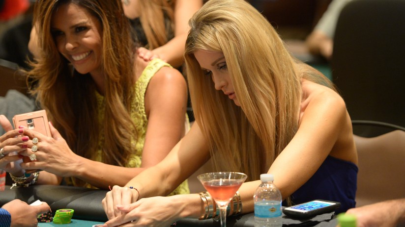 Close-up view of a poker table with playing cards, poker chips, and players engaged in a high-stakes game atmosphere.