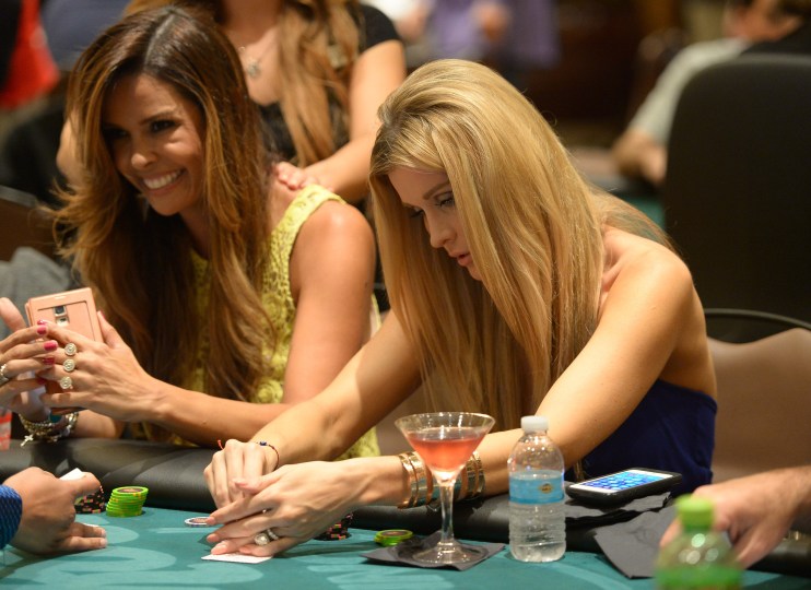 Close-up view of a poker table with playing cards, poker chips, and players engaged in a high-stakes game atmosphere.