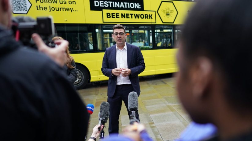 Andy Burnham discussing Bee Network devolution plan with city skyline in background