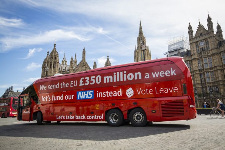 Red bus with Brexit misinformation slogan parked on a street, highlighting controversial political claims and public react...