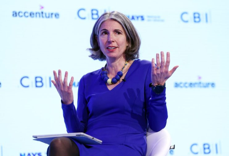 CBI Chief Economist Newton-Smith addressing economic trends at a business conference podium with charts in the background