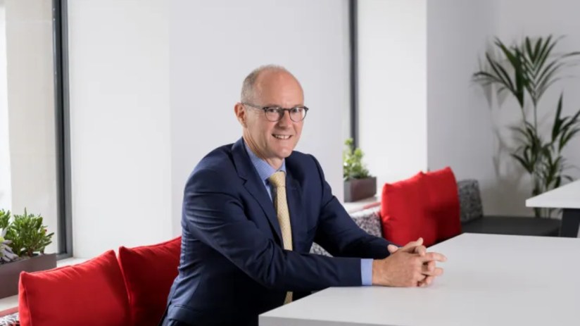 David Sleath, Chief Executive Officer, delivering a speech at a business conference with a focused expression.