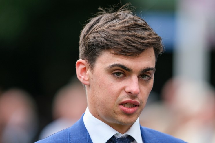 Donnacha OBrien confidently poses at a racetrack, showcasing his professional demeanor and equestrian attire.