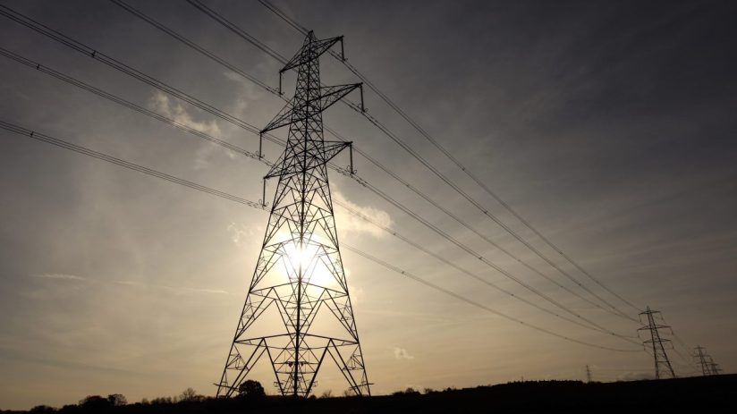 Electricity grid infrastructure with high-voltage power lines and pylons under a clear sky, representing energy distribution.
