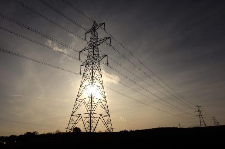 Electricity grid infrastructure with high-voltage power lines and pylons under a clear sky, representing energy distribution.