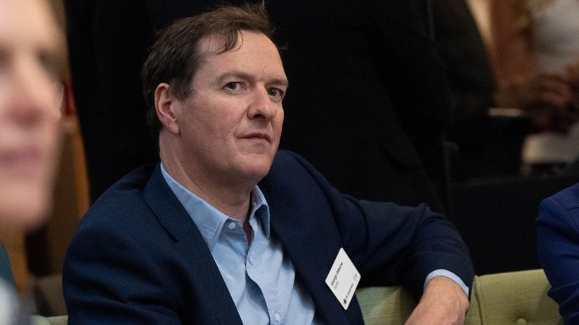George Osborne speaking at a business conference, wearing a suit, addressing economic issues and policy changes in the UK.