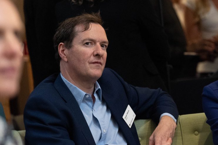George Osborne speaking at a business conference, wearing a suit, addressing economic issues and policy changes in the UK.