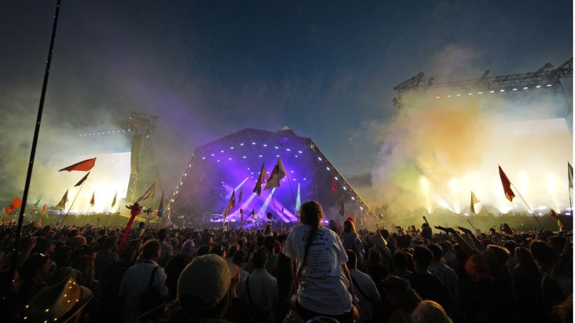 Aerial view of Glastonbury Festival showcasing vibrant crowds, colorful tents, and iconic Pyramid Stage under clear skies