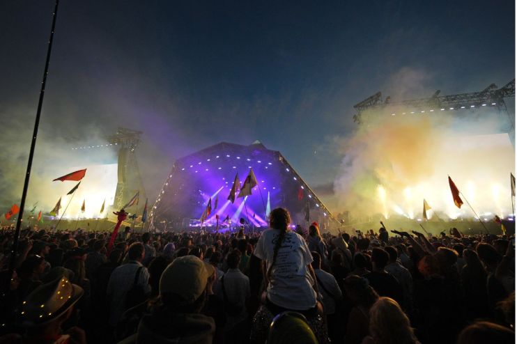 Aerial view of Glastonbury Festival showcasing vibrant crowds, colorful tents, and iconic Pyramid Stage under clear skies
