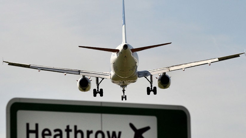Commercial airplane landing at Heathrow Airport, seen from behind, with a prominent Heathrow sign below.