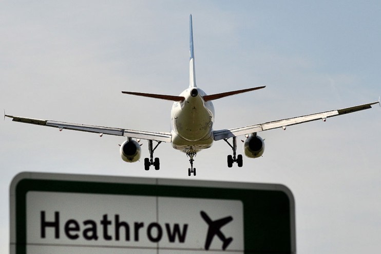 Commercial airplane landing at Heathrow Airport, seen from behind, with a prominent Heathrow sign below.