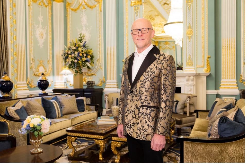 John Caudwell speaking at a business conference, dressed in a suit, gesturing with his hands, with a focused audience list...