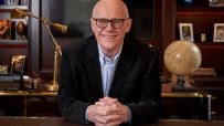 John Caudwell in a formal setting, possibly during a business meeting or public speaking event, conveying professionalism.