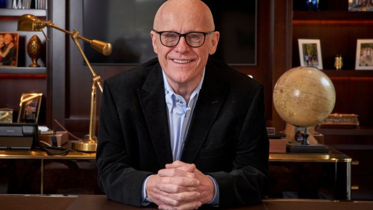 John Caudwell in a formal setting, possibly during a business meeting or public speaking event, conveying professionalism.