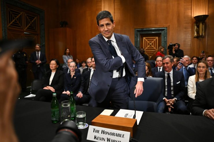 Kevin Walsh addressing a conference audience in a formal business setting, wearing a suit and gesturing with his hand.