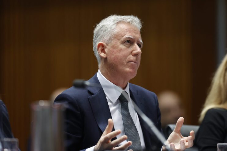 Martin Sheppard speaking at a business conference podium, wearing a suit, with a focused audience in the background
