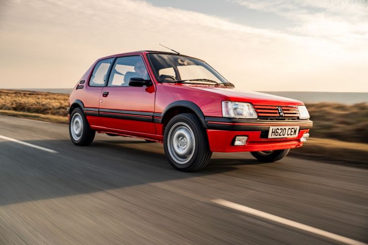 Vintage Peugeot 205 driving on a scenic road, showcasing classic design and compact size for a news feature on iconic cars