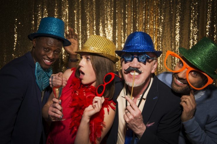 Friends taking photobooth selfies at a lively event, capturing joyful expressions and playful poses in a casual setting.
