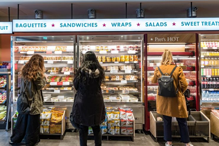 A busy Pret A Manger storefront with customers entering and exiting during lunchtime in a bustling city center.