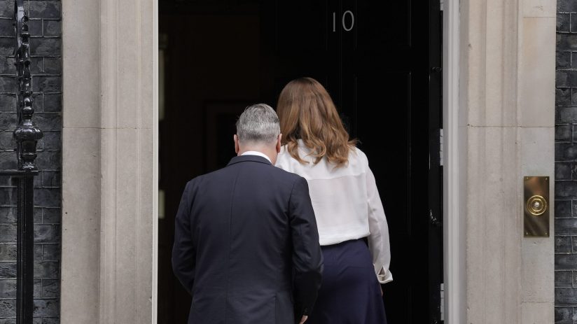 Keir Starmer standing near Number 10 Downing Street discussing political matters with media presence in the background