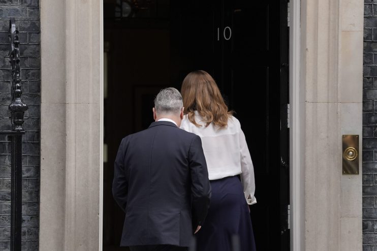 Keir Starmer standing near Number 10 Downing Street discussing political matters with media presence in the background