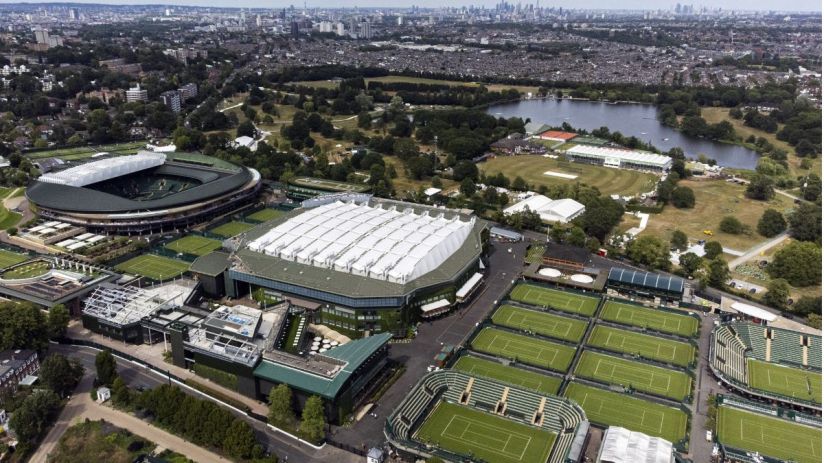Wimbledon tennis court with players in action, surrounded by a cheering crowd under clear blue skies