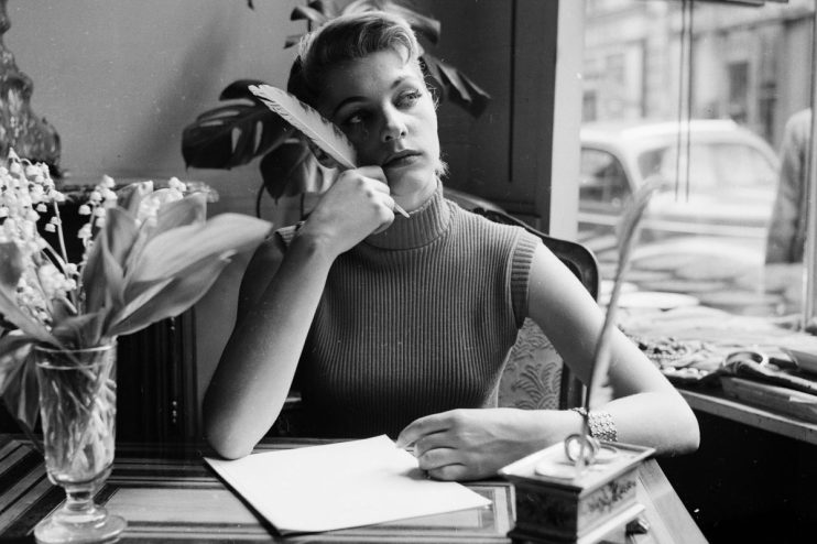 Writer working diligently at a desk, surrounded by notes and a laptop, focused on creating content for a news article.
