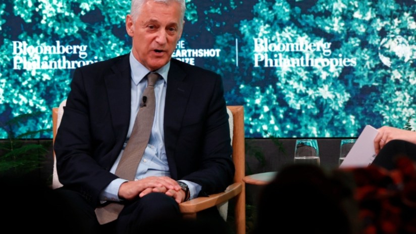 Standard Chartered CEO Bill Winters at an event, wearing a suit, speaking into a microphone against a corporate backdrop.