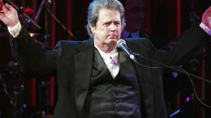 Brian Wilson performing live on stage, surrounded by musical instruments and colorful stage lights, captivating the audience