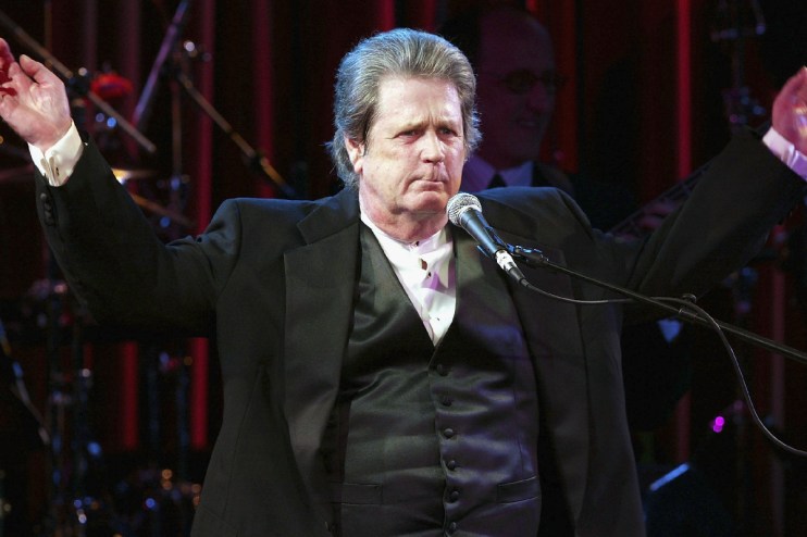Brian Wilson performing live on stage, surrounded by musical instruments and colorful stage lights, captivating the audience