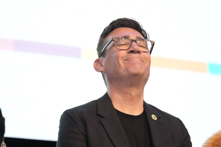Andy Burnham smiling at a public event, wearing a suit and tie, representing positive leadership and community engagement.