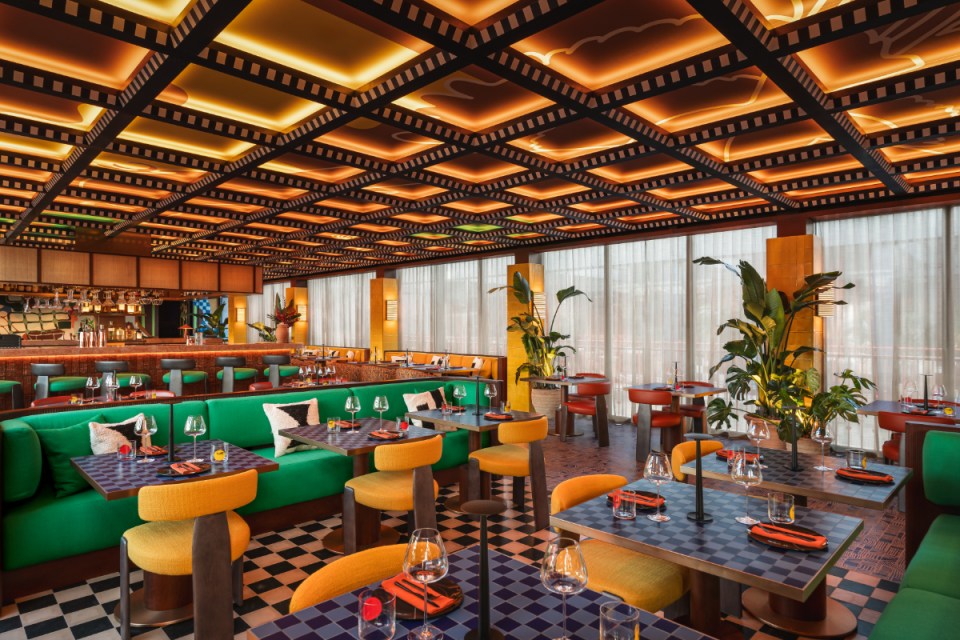 Interior view of a vibrant restaurant featuring green seating, colorful tables, and a ceiling designed with a film strip motif, illuminated by warm lighting.