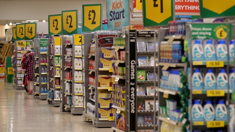 Customers shopping in a bustling supermarket aisle filled with fresh produce and grocery items.