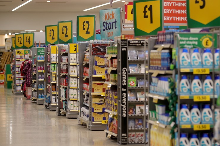 Customers shopping in a bustling supermarket aisle filled with fresh produce and grocery items.