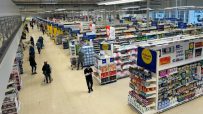 Overhead view of a brightly lit Tesco store interior with shoppers, product aisles, and Clubcard Prices signage.