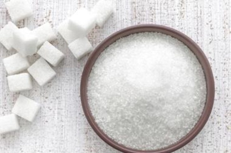 Sugar granules close-up on a wooden surface, highlighting texture and crystal structure, relevant to sugar industry news.