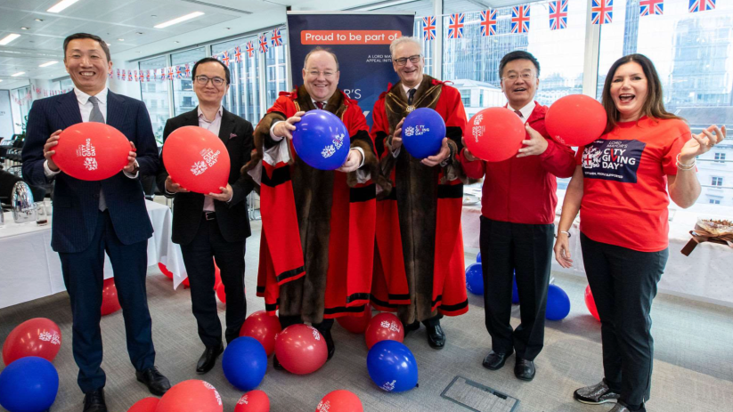 Group of aldermen and participants holding balloons at City Giving Day event, UK flags in background.