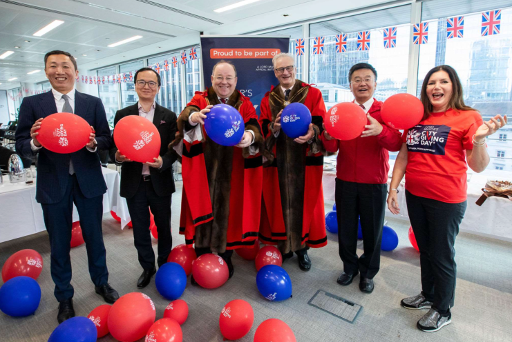 Group of aldermen and participants holding balloons at City Giving Day event, UK flags in background.