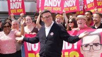 Andy Burnham speaking passionately at a public event, wearing a suit, highlighting his role as a prominent political figure.
