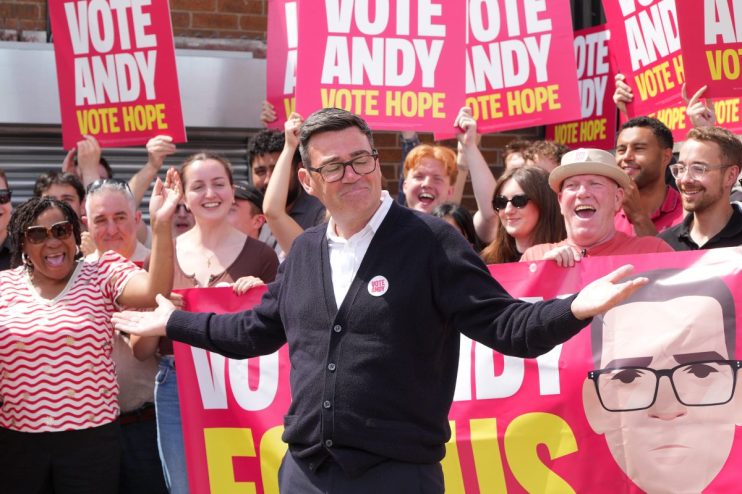 Andy Burnham speaking passionately at a public event, wearing a suit, highlighting his role as a prominent political figure.