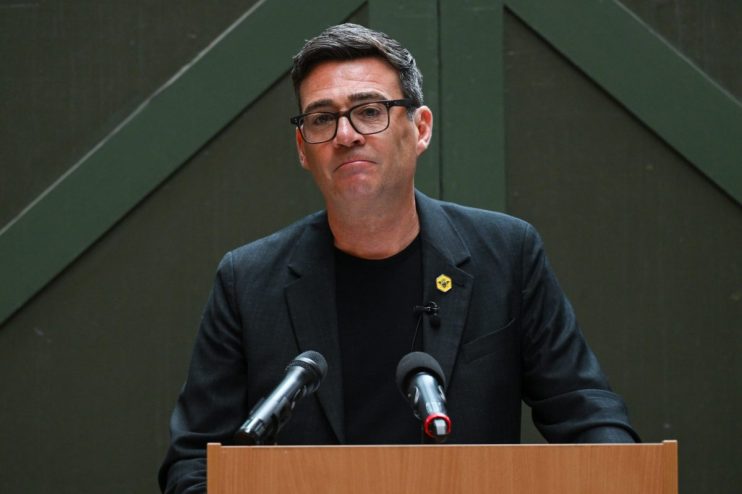 Andy Burnham speaking at a press conference, addressing current events and regional developments, wearing a suit and tie.