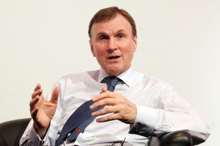 Archie Norman, business leader, speaking at a corporate event wearing a suit and tie, engaging with the audience.